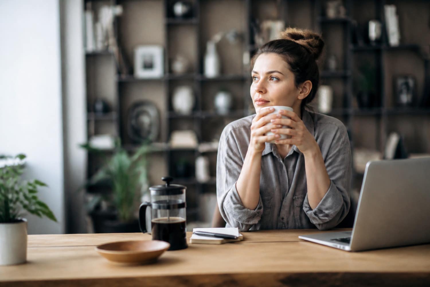 Tasse de café fumante posée sur un bureau en bois clair, avec un ordinateur portable ouvert et des documents légèrement éparpillés, suggérant le stress. La lumière est douce et naturelle, créant une ambiance studieuse.
